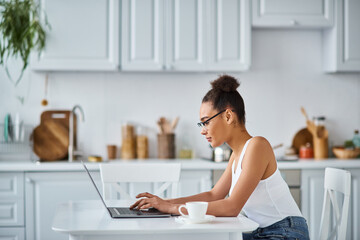 side view of curly african american woman in glasses working from home on her laptop, entrepreneur