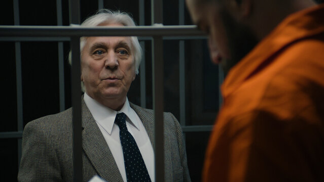 Lawyer talks with criminal in orange uniform standing in prison cell and offers his services. Prisoner serves imprisonment term for crime in correctional facility. Inmate in detention center or jail.