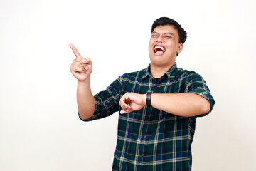 Young asian man laughing pointing sideways while checking time on his wrist watch