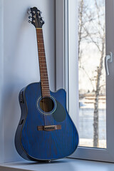 Dreadnought acoustic guitar is on window sill by the window.