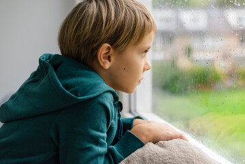 A boy looks out the window at a rainy street. Rainy weather.