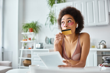 african american woman shopping online with tablet kissing credit card in hand near coffee aside