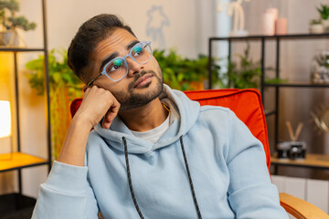 Portrait of sad Indian man guy sitting at home looks pensive thinks over life concerns or...