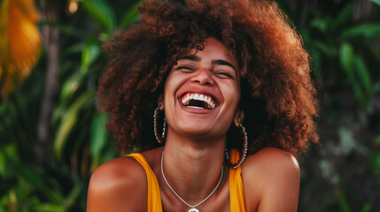 A radiant woman with a bright smile and voluminous curly hair enjoys a moment of genuine laughter amidst lush tropical greenery. This image captures the carefree joy and vitality of youth
