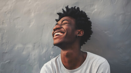 A young man's laughter fills the frame, set against a subtle gray background that accentuates his genuine happiness and relaxed demeanor.