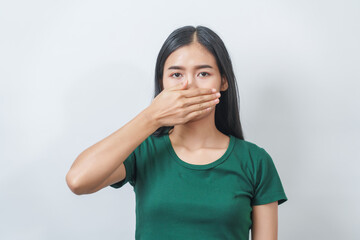 Young Asian frustrated woman with green t-shirt pinches her nose with disgust on her face, reacting...