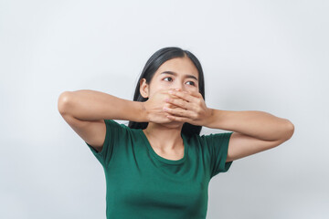Young Asian frustrated woman with green t-shirt pinches her nose with disgust on her face, reacting to a bad smell in isolation over background.