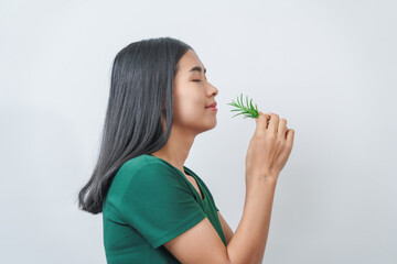 Young pretty Asian woman in a green t-shirt inhales the scent of the herbal rosemary isolated over...