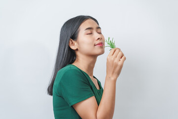 Young pretty Asian woman in a green t-shirt inhales the scent of the herbal rosemary isolated over...