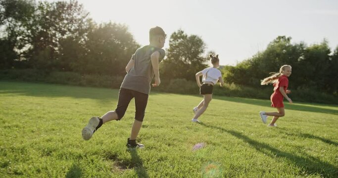 Exuberant Teens Playing Tag on Grassy Field at Dusk in Slow Motion