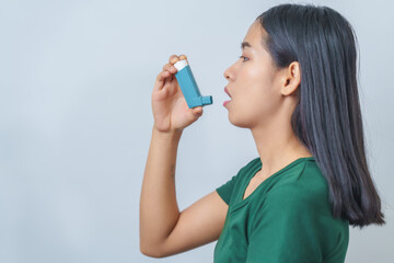 Young Asian woman wearing green t-shirt using asthma inhaler isolated on white background, indoors, studio shot.