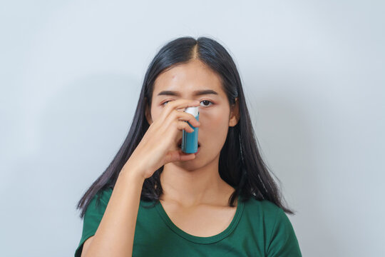 Young Asian woman wearing green t-shirt using asthma inhaler isolated on white background, indoors, studio shot.