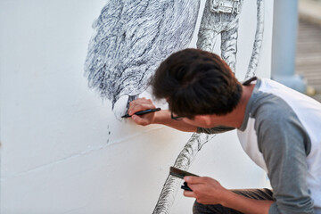 Young male painter passionately paints picture with black permanent marker for outdoor street...