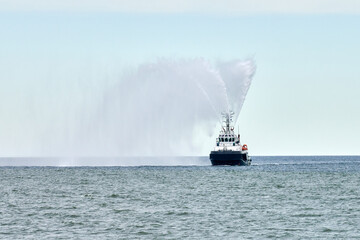 Fireboat ship sails on open sea directing jets of water to sides demonstrating bravery water...