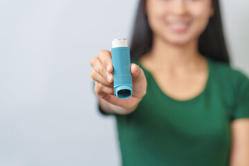 Young Asian woman wearing green t-shirt using asthma inhaler isolated on white background, indoors, studio shot. - obrazy, fototapety, plakaty
