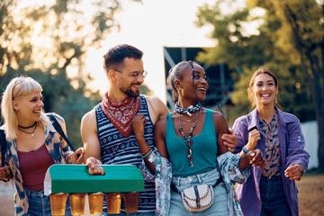 Multiracial group of happy friends with package of draft beer going to open air music concert...
