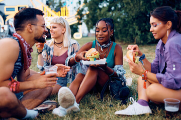 Multiracial group of friends eating hamburgers and drinking beer while attending open air music...