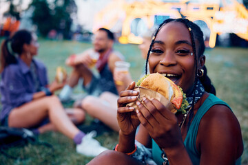 Hungry black woman eating hamburger during open air music festival in summer.
