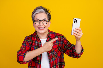 Portrait of positive grandmother indicate finger hand hold apple iphone gadget isolated on yellow color background