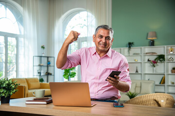 Indian Mid age man working on laptop, smartphone with documents having coffee - Powered by Adobe
