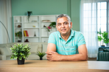 Indian middle aged man sitting across table looking at camera with smile