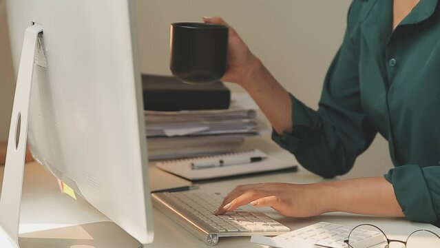 Beautiful young smiling Asian businesswoman working on laptop and drinking coffee, Asia businesswoman working document finance and calculator in her office.