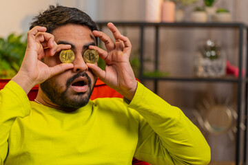 Indian man freelancer holding two gold coins, successful developer programmer. Guy stock trader...