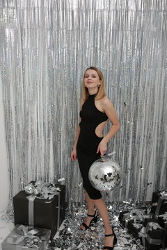 foil rain curtain. beautiful girl in a black dress New Year's photo .mirror disco ball and silver confetti. Festive splash background with shining sparkles. Silver glass disco ball. Party atmosphere 