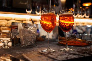 Two glasses of cocktail Aperol spritz on bar counter. Making typical alcoholic italian beverage, aperitif made with Prosecco sparkling white wine, ice and fresh orange slices. Mixing orange liquid.