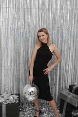 Naklejka premium foil rain curtain. beautiful girl in a black dress New Year's photo .mirror disco ball and silver confetti. Festive splash background with shining sparkles. Silver glass disco ball. Party atmosphere 