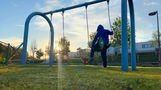 Ni&ntilde;o feliz y divertido corre hacia el columpio para disfrutar de una fr&iacute;a ma&ntilde;ana al amanecer aprovechando los juegos del parque al aire libre al exterior disfrutando su infancia
