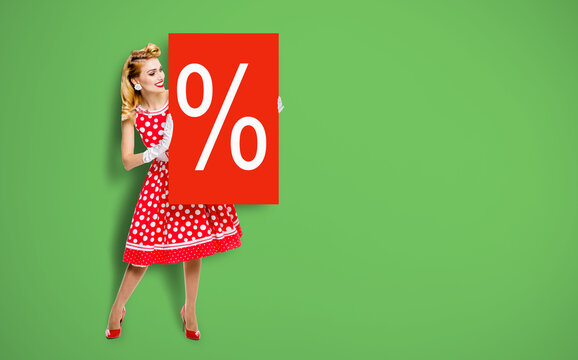 Beautiful woman wear pinup dress hold, show red board percents % sign. Full body pin up girl with advertise offer, isolated against green background. Sales, discounts, rebates ad concept.