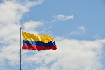 Bandera de Colombia sobre fondo de cielo azul despejado, espacio para texto al lado derecho. - obrazy, fototapety, plakaty