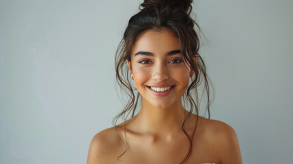 Obraz premium A cheerful young woman stands with her hair tied up and smiles widely against a white background