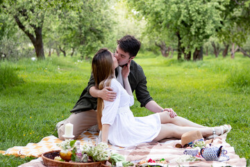 young couple on a picnic in summer park, eating strawberries and kissing