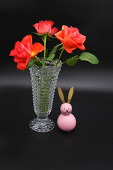 Image of a vase with red flowers, pink hair, dark background.