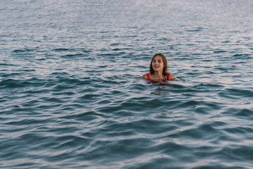 A young woman with a smile on her face is swimming in the calm ocean waters during the early...