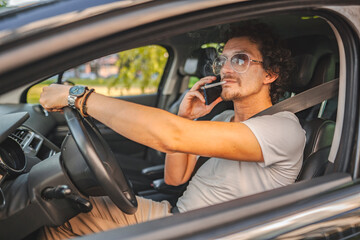 Man with curly hair driving a car, smoking a cigarette and using phone