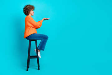Full body profile portrait of pretty nice lady sit stool arms hold empty space isolated on turquoise color background - obrazy, fototapety, plakaty