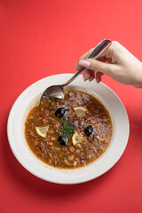 Soup with meat, tomato and olives on a red background