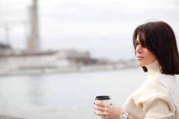 A girl with a stylish bob haircut is walking around the city, drinking coffee against the...