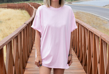 Young girl wearing blank oversized pink t shirt , pink t shirt mock up , pink tshirt for your rustic wooden  shirt design
