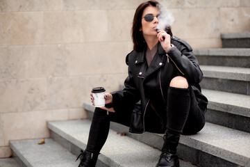 A beautiful girl with a stylish bob haircut is walking around the city, drinking coffee or tea....