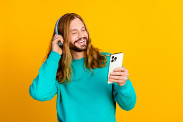 Portrait of excited young man hand touch headphones use smart phone empty space isolated on yellow...