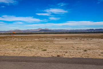 Arid landscape at international airport with an orange weather vane, mountains against blue sky in...