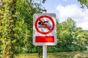 Sign post prohibiting swimming at Lake Echternach, green leafed trees against blue sky in background, sunny summer day in Luxembourg