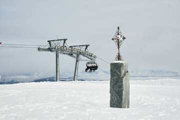 Krzyż w górach. W tle wyciąg narciarski i narciarze. Śnieg, zima, białe szaleństwo.