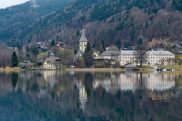 Kościół z klasztorem w górskiej miejscowości nad jeziorem. Odbicie fasady w wodzie. gładka tafla jeziora. W tle góry i lasy.