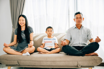 Calmness and family bonding as parents and their young son practice yoga on a sofa. Illustrating...