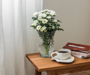 A cup of coffee, a bouquet of chrysanthemums, books on a wooden bench in the living room